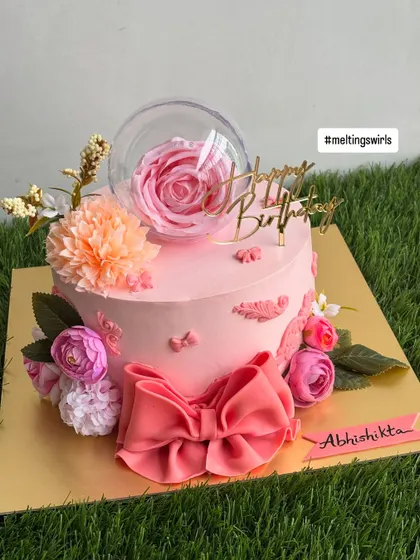 This view shows the beautiful composition of the pink floral cake, with its delicate bow, flowers, and elegant "Happy Birthday" topper.