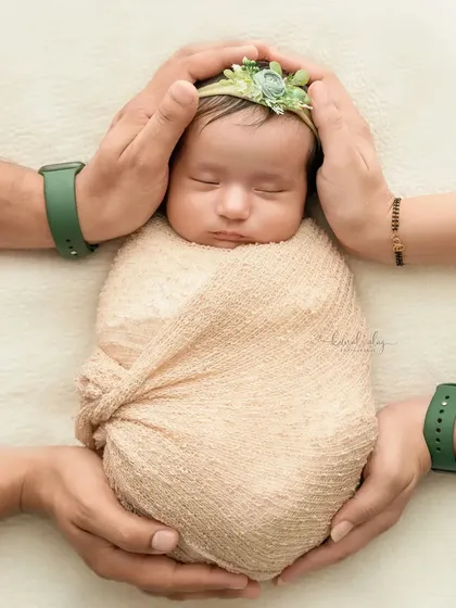 A close-up of a newborn's head and torso being cradled by their parents' hands.