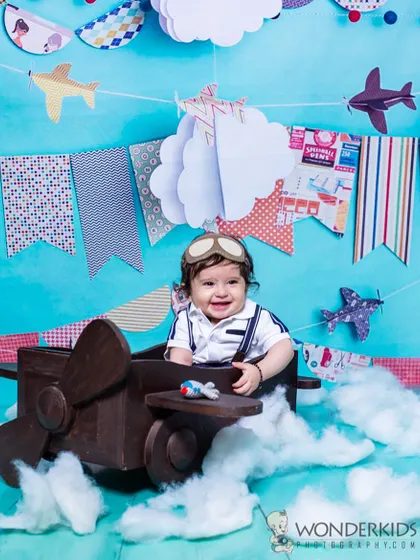 A smiling baby boy enjoying his flight in our airplane-themed setup. The handmade clouds and colorful banners add to the adventurous and celebratory feel of the photoshoot.