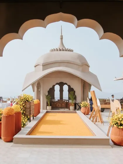 The entrance to the 'Jaipur Wali Haldi', framed by a traditional Rajasthani arch. The path is lined with marigold flowers, setting a festive and welcoming tone for the Mela-themed celebration.