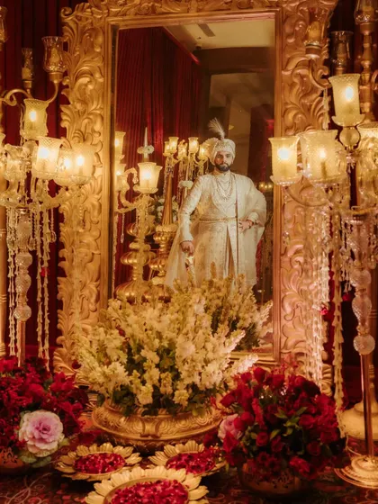 An artistic shot of the groom, Akshay, reflected in a mirror amidst grand, golden decor, creating a majestic and layered portrait.