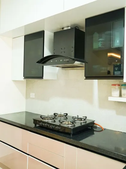 A contemporary kitchen design featuring blush pink lower cabinets and white upper cabinets with dark, smoked glass fronts. The black granite countertop and minimalist handles create a chic and sophisticated look.