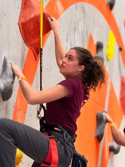 A female competitor focuses on her next move during the Speed Climbing event. This competition requires explosive power and precise, efficient movement to get the fastest time.