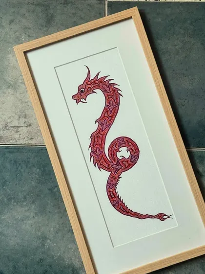 This framed piece showcases a dragon rendered in a style reminiscent of Indian folk art. The intricate patterns and bold red colour make it a striking addition to any art collection.