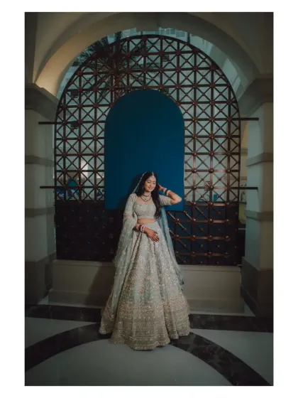 A stylish bridal portrait against a modern, arched doorway. The bride's pose is confident and elegant, showcasing her beautiful lehenga.