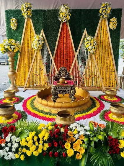 A traditional Haldi seating area with a backdrop of marigold strings arranged in geometric patterns against a green wall.