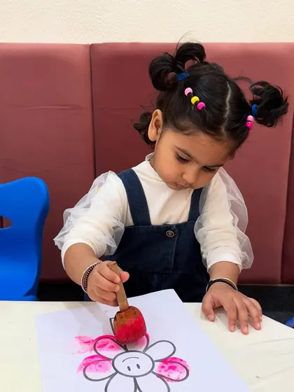 A child uses a sponge to dab pink paint onto a flower drawing. This simple stamping technique is great for developing hand-eye coordination and exploring color in a fun, tactile way.