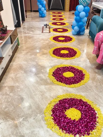 A walkway decorated with circular flower rangolis and balloon pillars to welcome a new baby home.