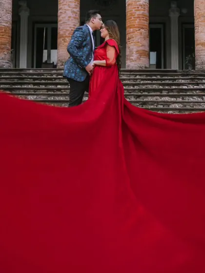 A tender kiss on the forehead, with the massive red trail of the gown filling the foreground. This shot is all about grand romance and intimacy.