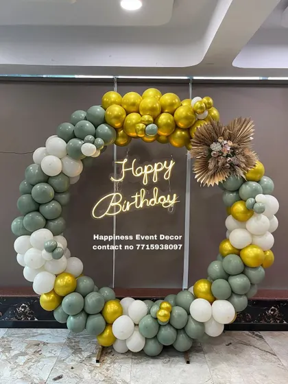An elegant balloon ring decoration with sage green, white, and gold balloons. The arrangement is finished with a small bouquet of dried pampas grass for a modern, bohemian look.