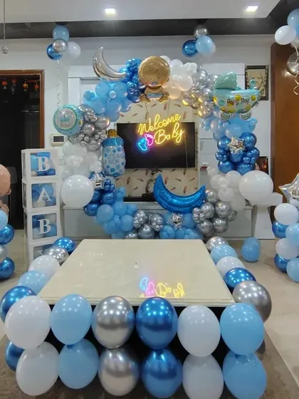 An elaborate living room setup for a 'Welcome Baby' party, with balloons decorating the center table and a large circular balloon arch in the background.
