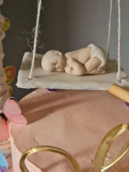 A close-up of the sleeping baby figurine from the swinging cradle cake. Every detail, down to the folds in the diaper, is sculpted by hand.