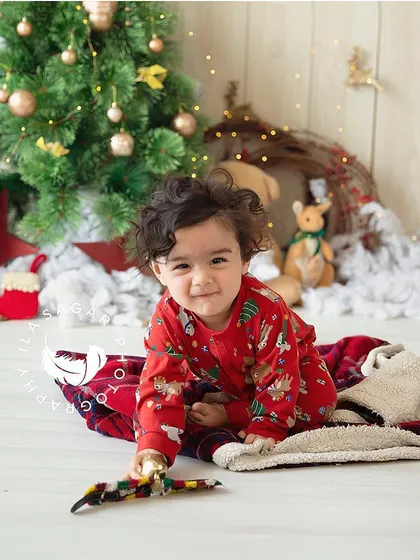 This little one is all smiles during his holiday-themed sitter session, surrounded by a Christmas tree and festive decorations.