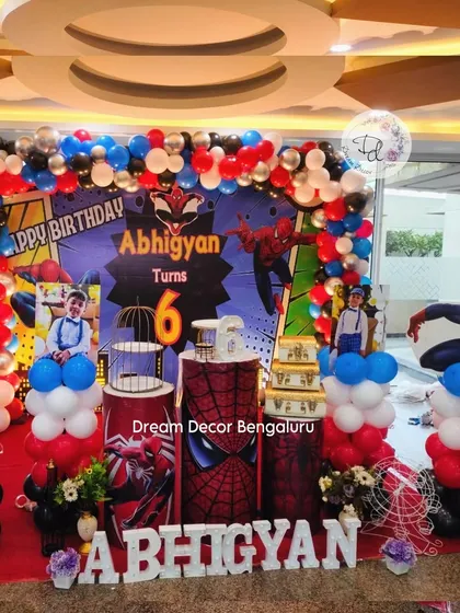 This Spider-Man theme is perfect for a young superhero's birthday. The backdrop features the iconic web-slinger in action, surrounded by a red, blue, and black balloon arch and themed cake stands.