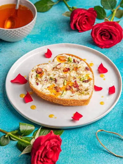 A heart-shaped Ghewar, beautifully decorated with rabri, rose petals, and nuts. A stunning dessert that tastes as good as it looks.
