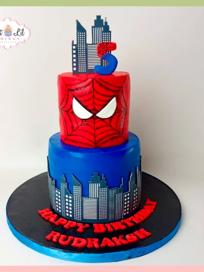 A two-tiered Spider-Man cake for a 5th birthday. The top tier features Spidey's mask, while the bottom tier shows a city skyline, creating a dynamic superhero scene.