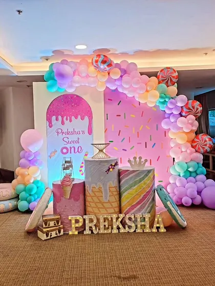 Preksha's "Sweet One" birthday was a candyland dream. This setup features a sprinkle backdrop, a gumball machine prop, and a pastel balloon arch with candy-shaped balloons.
