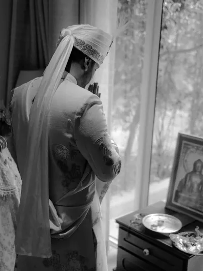 A quiet moment of prayer for the groom before the ceremony begins, a beautiful black and white shot capturing tradition and reflection.