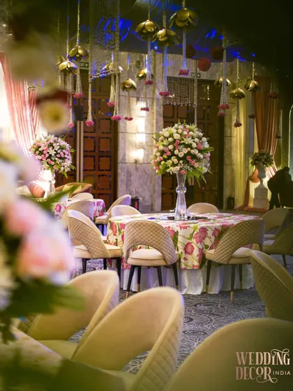A close-up of a dining table at the Sufi-inspired wedding. The floral-printed tablecloth is paired with a tall, elegant centerpiece of pink and white roses.