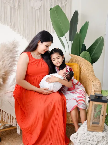 A heartwarming newborn session featuring a mother, her older daughter, and the new baby. The older sister gently holds the newborn, capturing a beautiful moment of sibling connection.