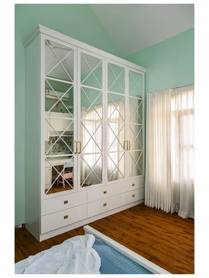 A classic white wardrobe with mirrored, cross-patterned doors, adding elegance and reflecting light in this daughter's bedroom.