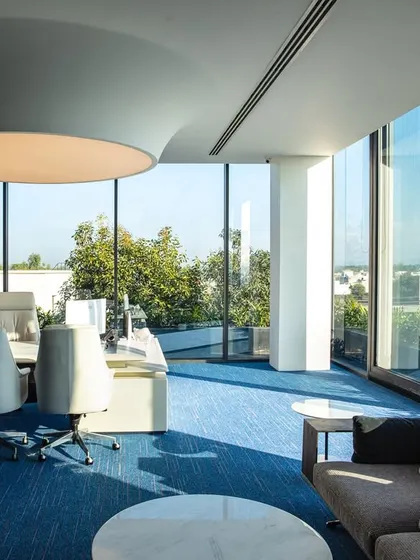 Natural light is a key element in my office designs. This executive office is enveloped in floor-to-ceiling glass, offering panoramic views and creating a bright, energizing atmosphere, complemented by a large, modern ceiling light that serves as a functional centerpiece.