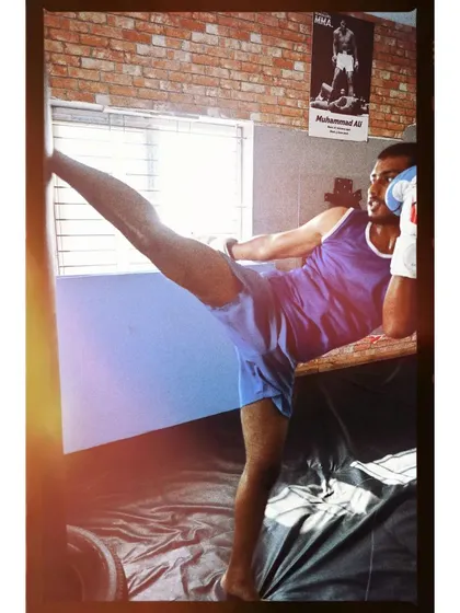 A fighter practicing his high kick, inspired by the great Muhammad Ali on the poster behind him. We draw motivation from the legends of combat sports.