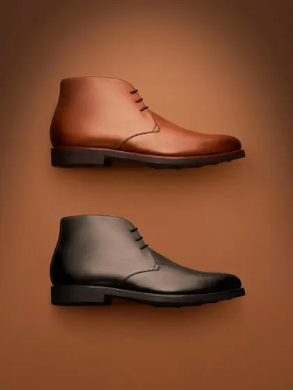 A clean, graphic composition for Hanker Boots. Placing the brown and black boots against a simple, gradient background isolates them and allows the viewer to focus purely on their classic shape and form.