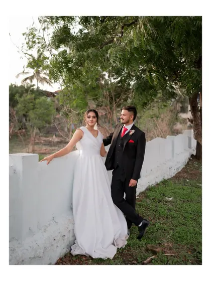 A stylish portrait of the bride and groom posing by a white wall outdoors after their church wedding.