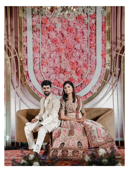 A classic, formal portrait of a couple seated against a beautiful pink floral backdrop at their reception.