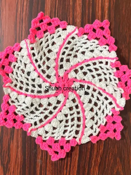 A star-shaped crochet doily in white and pink, with a swirling pattern that creates a sense of movement.