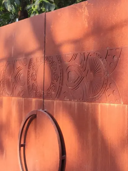 A detail of the corten steel gate, showing the custom circular handle and the intricate, nature-inspired patterns etched into the metal.