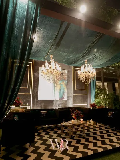 A wider shot of the teal velvet cabana, showing how it creates a defined, intimate zone within the larger outdoor venue, complete with its own chandeliers.