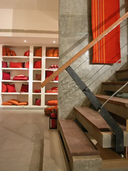 Inside the Yamini store, we contrasted raw concrete walls with warm wood and the brand's vibrant textiles. A simple, robust staircase connects the floors, while built-in shelving provides a clean, organized backdrop for the colorful home furnishing products.