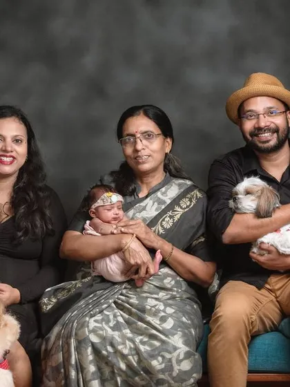 A full family portrait that includes everyone. The parents, grandmother, newborn, and their two dogs, a Golden Retriever and a Shih Tzu, all pose together.