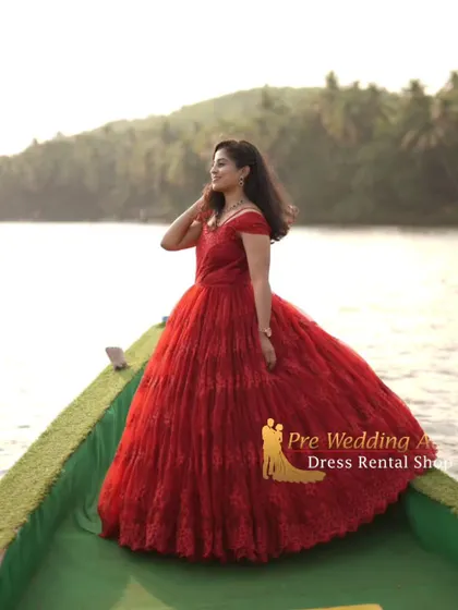 The red lace ball gown looks stunning in this waterside shot, with the full skirt creating a beautiful silhouette against the open background.