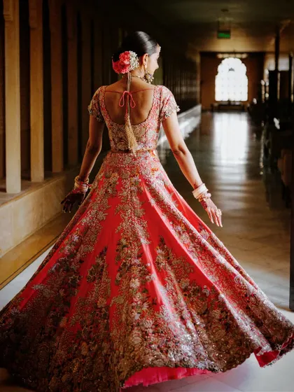 A back view of the bride's intricately embroidered lehenga and her elegant floral hair bun, highlighting the detailed craftsmanship of her wedding look.