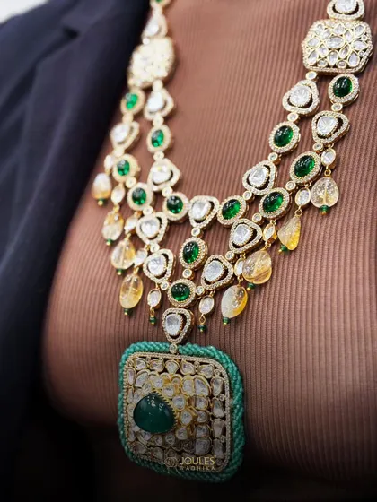 The cascading layers of this bridal necklace create a sense of grandeur. The combination of large polki stones and vibrant green emeralds makes it a statement piece for any bride.