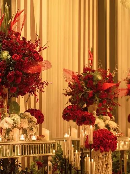A console table laden with an abundance of red florals in varying heights and textures. The mirrored table reflects the candlelight, amplifying the warmth and richness of the display.