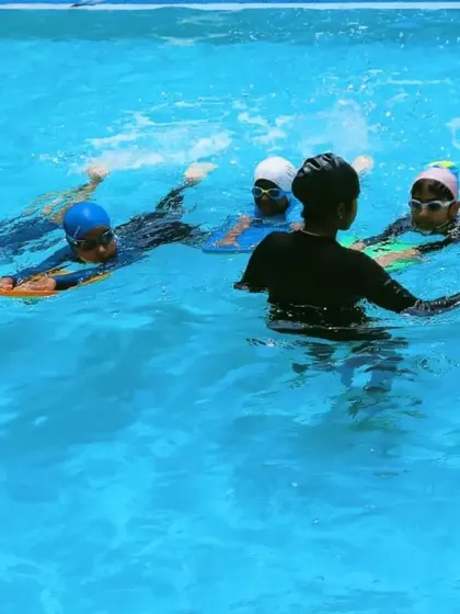 A group of beginner swimmers practices kicking with kickboards under the watchful eye of their instructor. Using equipment like this helps isolate and strengthen specific muscle groups for better technique.