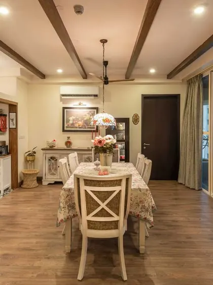 This dining space opens up to a large balcony, allowing for plenty of natural light. The design combines a classic white dining set with industrial ceiling beams for a unique stylistic blend.