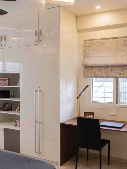 This bedroom features a custom wardrobe with an integrated study desk and open shelving. The glossy white finish makes the room feel bright and spacious, while the design maximizes functionality.