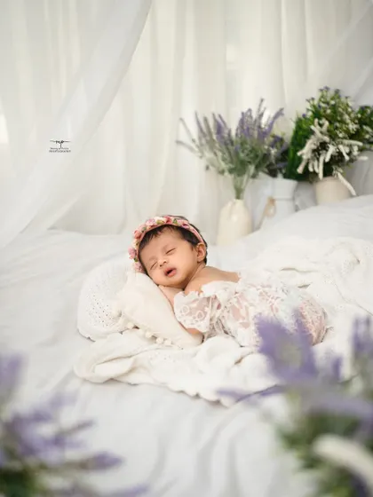 A newborn rests peacefully in a bed of soft white linens, framed by delicate lavender flowers. This lifestyle newborn photography approach creates a natural and timeless portrait.