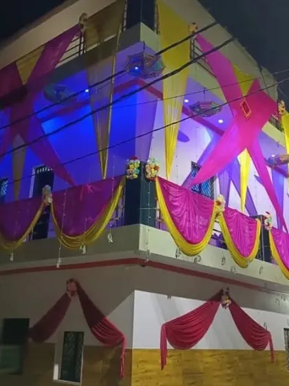 A house facade decorated at night with pink and yellow drapes in a criss-cross pattern, illuminated by blue and purple lights.
