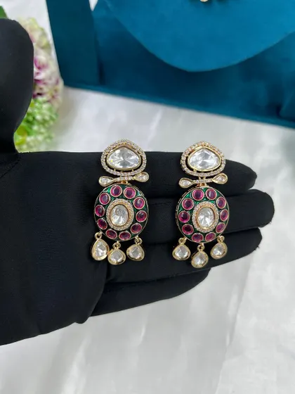 A pair of Moissanite Kundan earrings with a circular design. The ruby-colored stones and white stone drops make these a vibrant and attractive choice.
