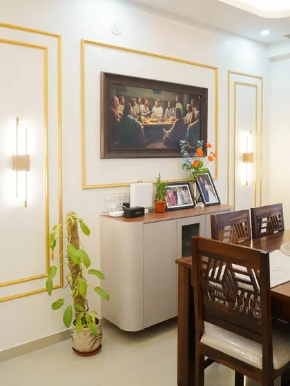 Elegance is defined by thoughtful details. This dining area features a classic wooden table set against a wall with decorative gold-trimmed paneling and modern sconce lighting, creating a perfect setting for family meals.
