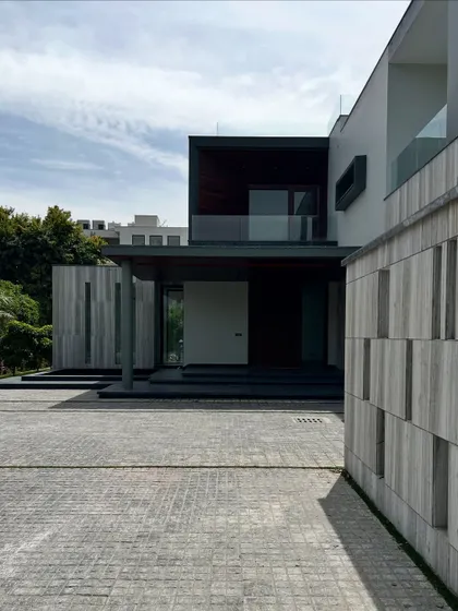 The entrance of Rosewood Farmhouse is a composition of strong geometric forms. The projecting balcony, the covered porch, and the textured boundary wall create a layered and dynamic facade that makes a lasting first impression.