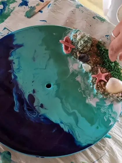 The final details make all the difference! Here, tiny shells, starfish, and moss are being added to a resin beach clock to complete the scene.