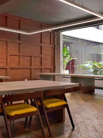 The VIP dining lounge at Campus Biovet, featuring a raw and natural material palette. An exposed brick wall, Kota stone floors, and a long exposed cement dining table create a unique, light-filled space.