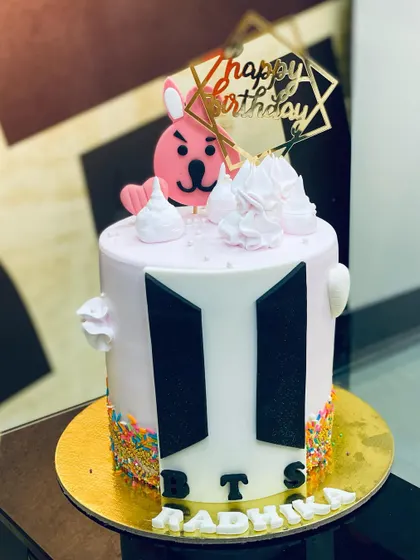 A 1.5kg BTS-themed cake with the iconic logo, sprinkles, and a cute character topper.